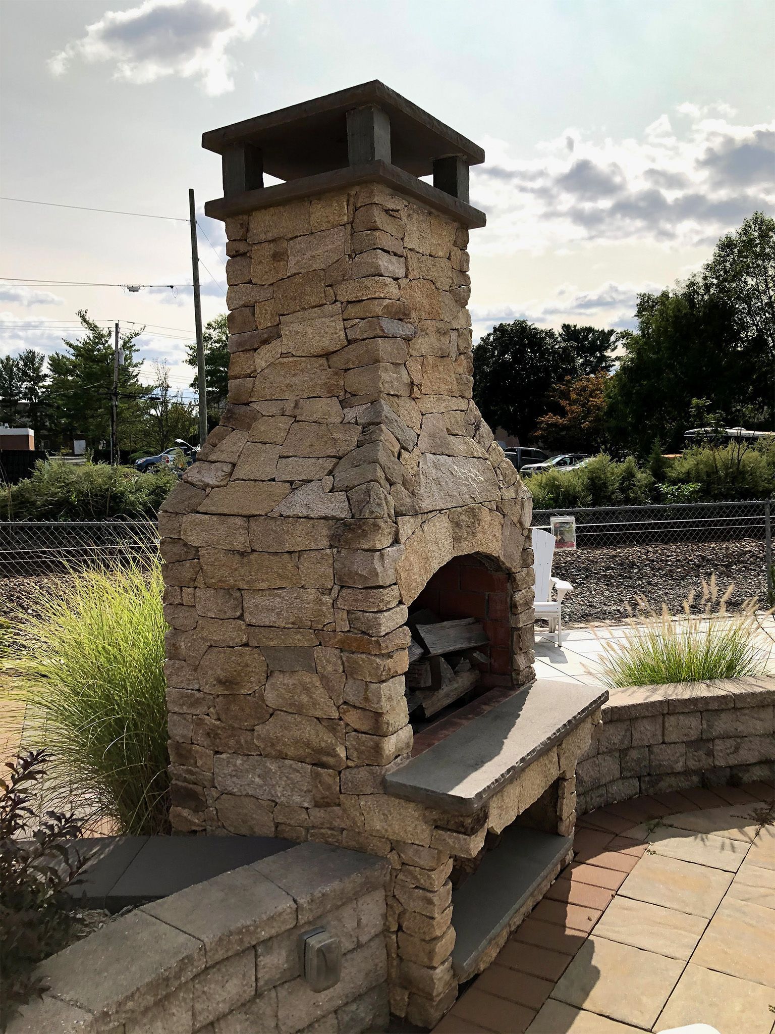 Stone outdoor fireplace with a bench, set on a tiled patio under a cloudy sky