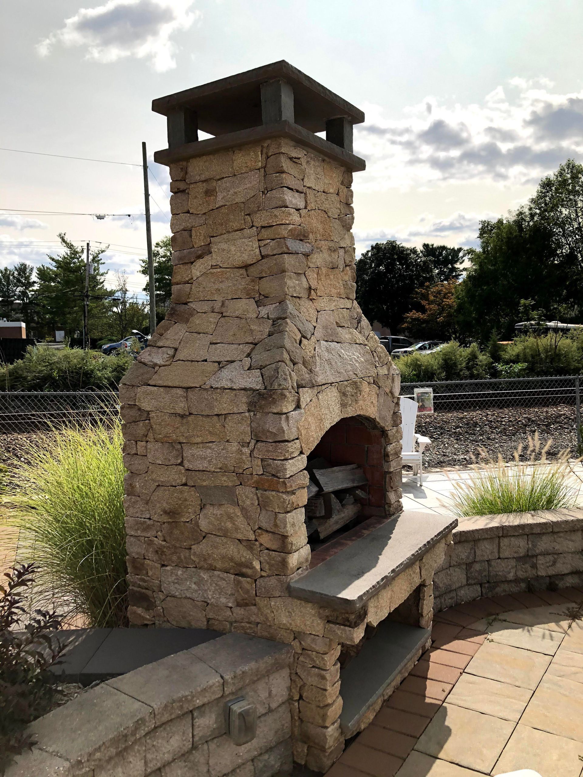Stone outdoor fireplace with arched opening and bench seating in a landscaped plaza