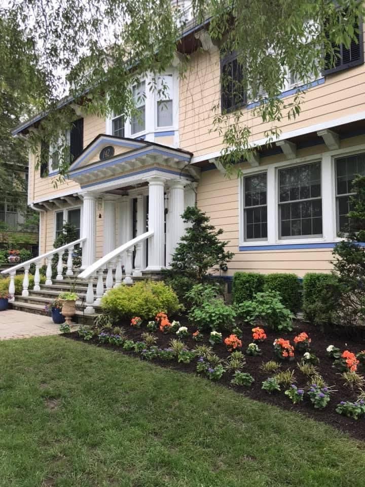 Two-story house with beige siding, white porch, and flower bed along the front lawn