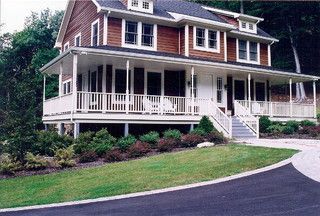 Large white two-story house with a wraparound porch, red siding, and landscaped front yard.