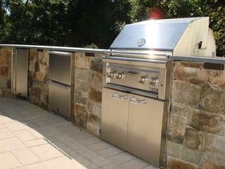 Outdoor stone-built barbecue and counter with stainless steel grill on a paved patio.