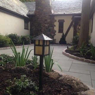Courtyard walkway with stone pillar, landscape lights, and potted plants beside a stucco building