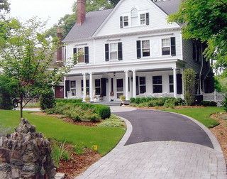 White two-story house with a curved stone driveway, front porch, and landscaped yard.