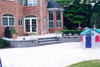 Brick house patio with steps and a small blue-and-pink playhouse on a paved yard
