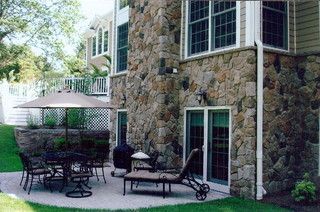 Stone patio with outdoor chairs, table, and umbrella beside a house with a large window and sliding door