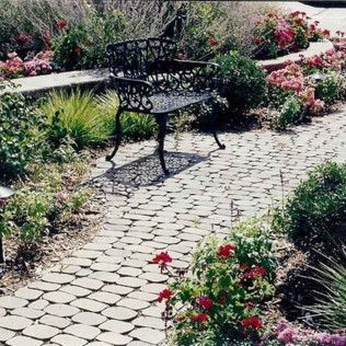 Garden bench on a cobblestone path surrounded by colorful flowers and greenery