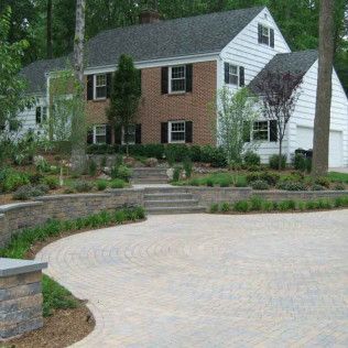 Brick house with white siding, stone steps, and a curved paved driveway surrounded by landscaped greenery