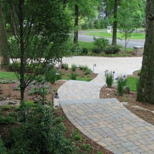 Curved brick walkway through a green landscaped garden beside a road