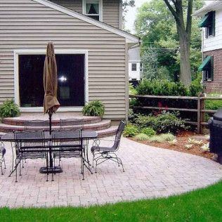 Patio with metal table and chairs, brown umbrella, and potted plants beside a house