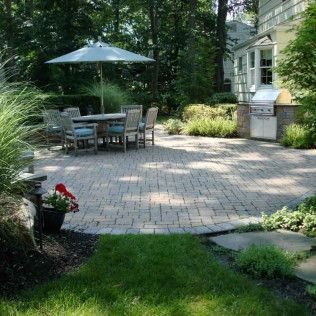 Backyard patio with dining table, umbrella, grill, and lush greenery
