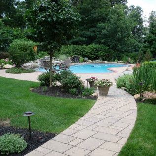 Curved stone path leads through a lush garden to a blue backyard swimming pool.