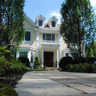 Large white house with two dormer windows and a front porch behind a curved driveway