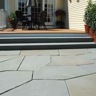 Patio with outdoor table and chairs on a wooden deck above a stone-paved patio with steps