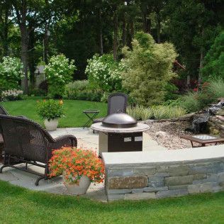 Backyard patio with fire pit, chairs, orange flowers, and a stone retaining wall surrounded by greenery
