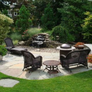 Backyard patio with wicker chairs around a fire pit, stone pathway, and small waterfall garden feature