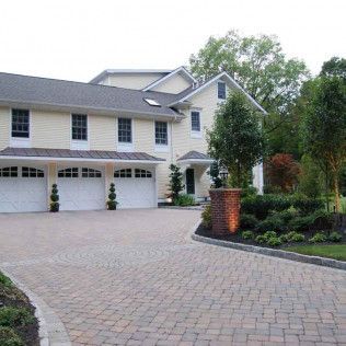 Large beige two-story suburban house with three-car garage and brick driveway in a landscaped front yard