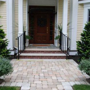 Front entry with brick walkway, steps, and a dark wooden door framed by white siding.