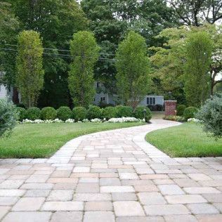 Curved stone path through a manicured garden with tall trees and green lawn leading to a house