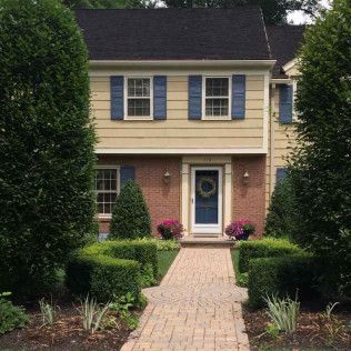 Two-story house with blue shutters, brick porch, and a brick walkway through a manicured front garden