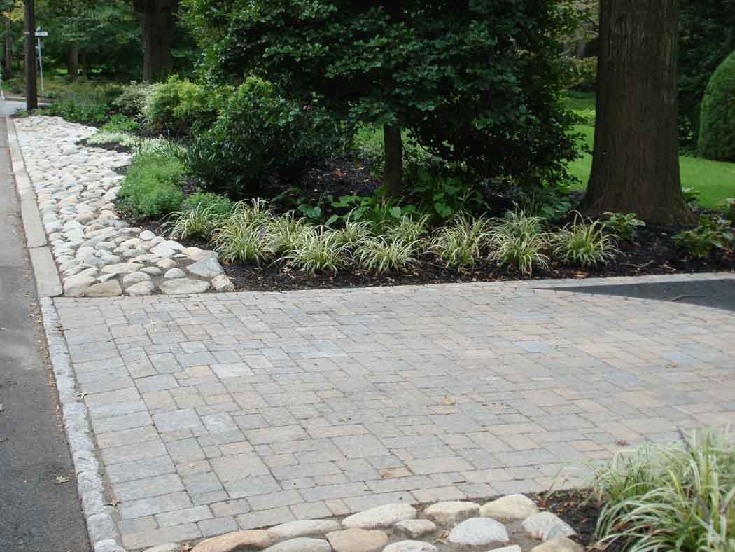 Paved garden path bordered by rocks and plants beside a lawn and trees