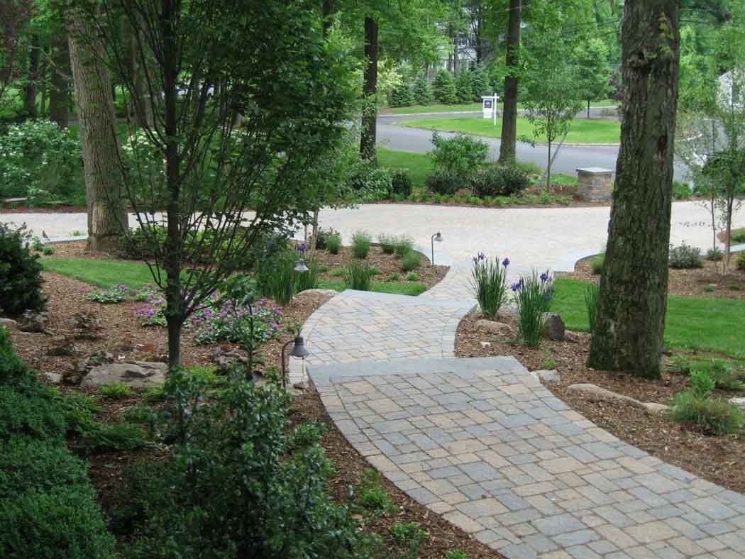 Curved stone walkway through a green landscaped garden with trees and shrubs