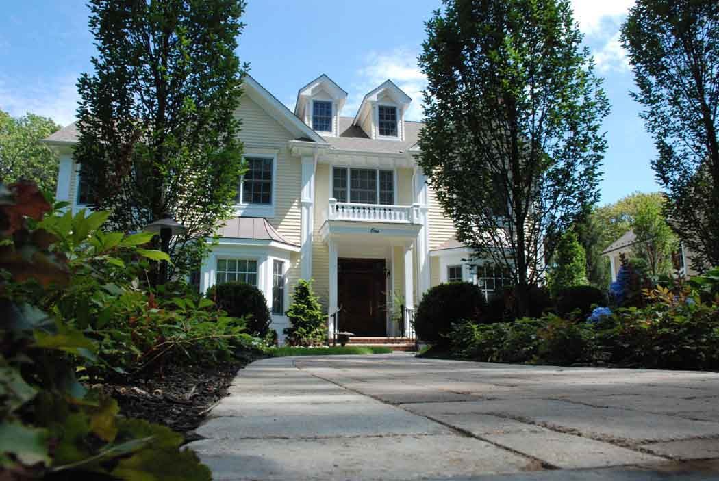 White two-story house with dormer windows, front porch, and tree-lined driveway