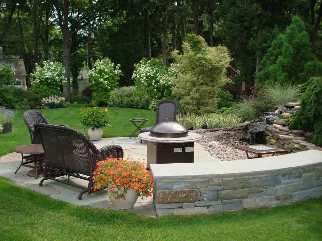 Backyard patio with fire pit, black chairs, orange flowers, and lush green landscaping
