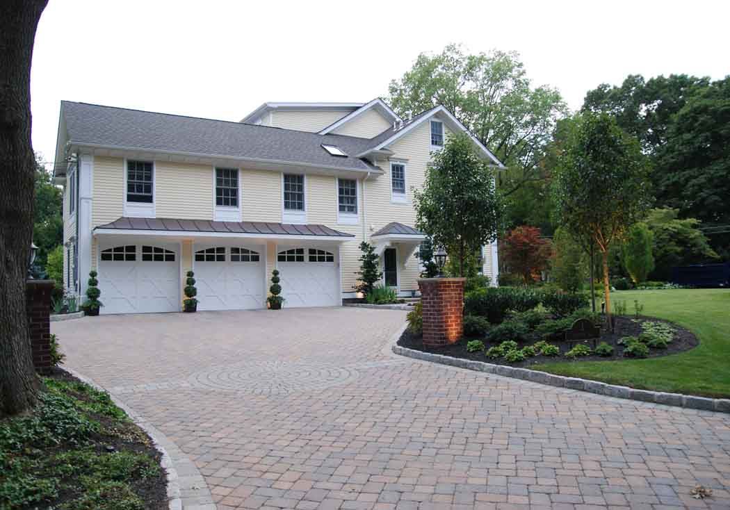 Two-story suburban house with three-car garage, paver driveway, and landscaped front yard