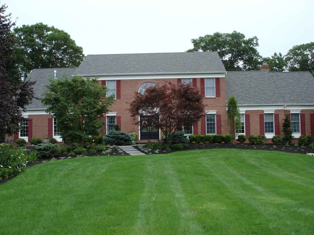 Large red-brick suburban house with white trim, gray roof, and a wide green lawn
