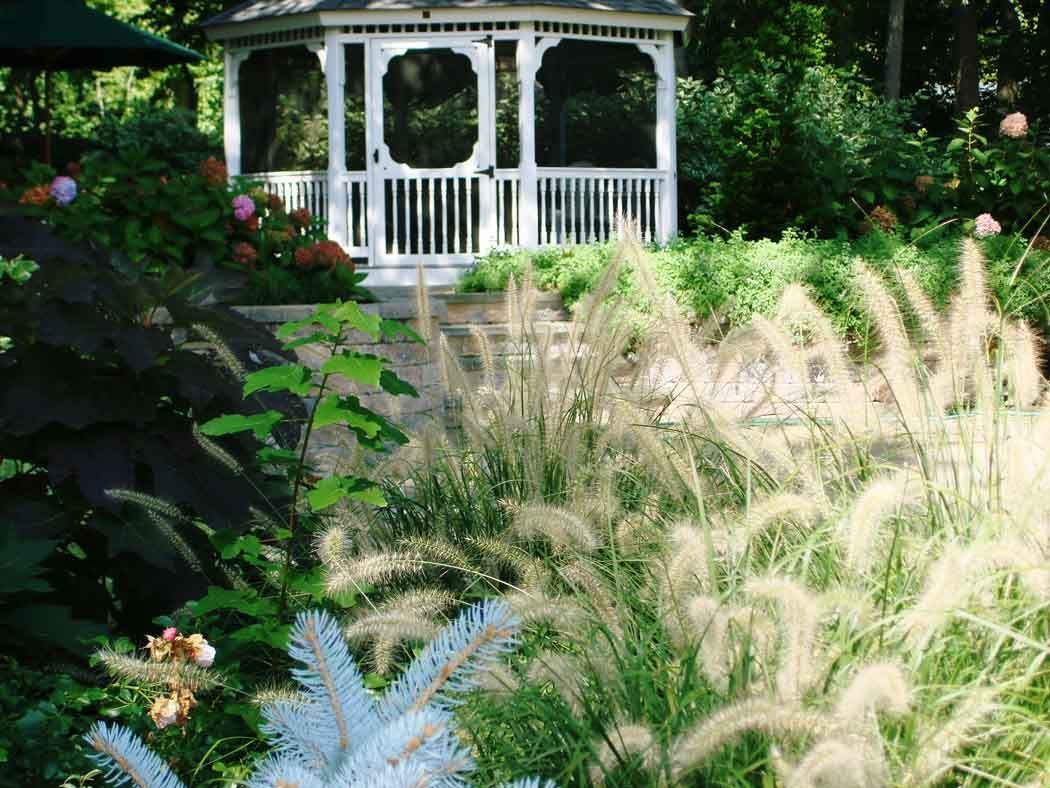 White gazebo in a lush garden with tall grasses and flowers in the foreground