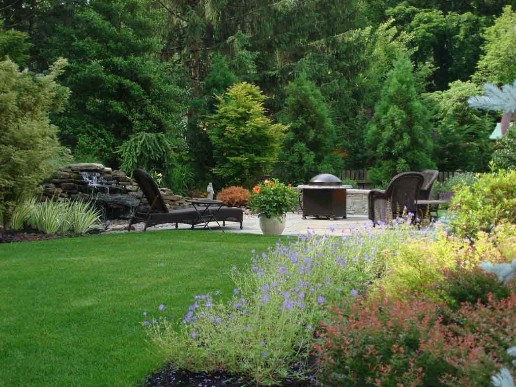 Lush garden patio with lounge chairs, grill, and colorful flower beds beside a green lawn