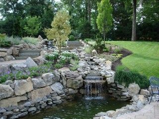 Rock garden waterfall and pond with lush green lawn and trees