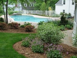 Backyard garden with a turquoise swimming pool, lawn, flower beds, and a white fence