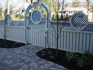 White vinyl fence with arched lattice gate and round blue insets beside a paved walkway