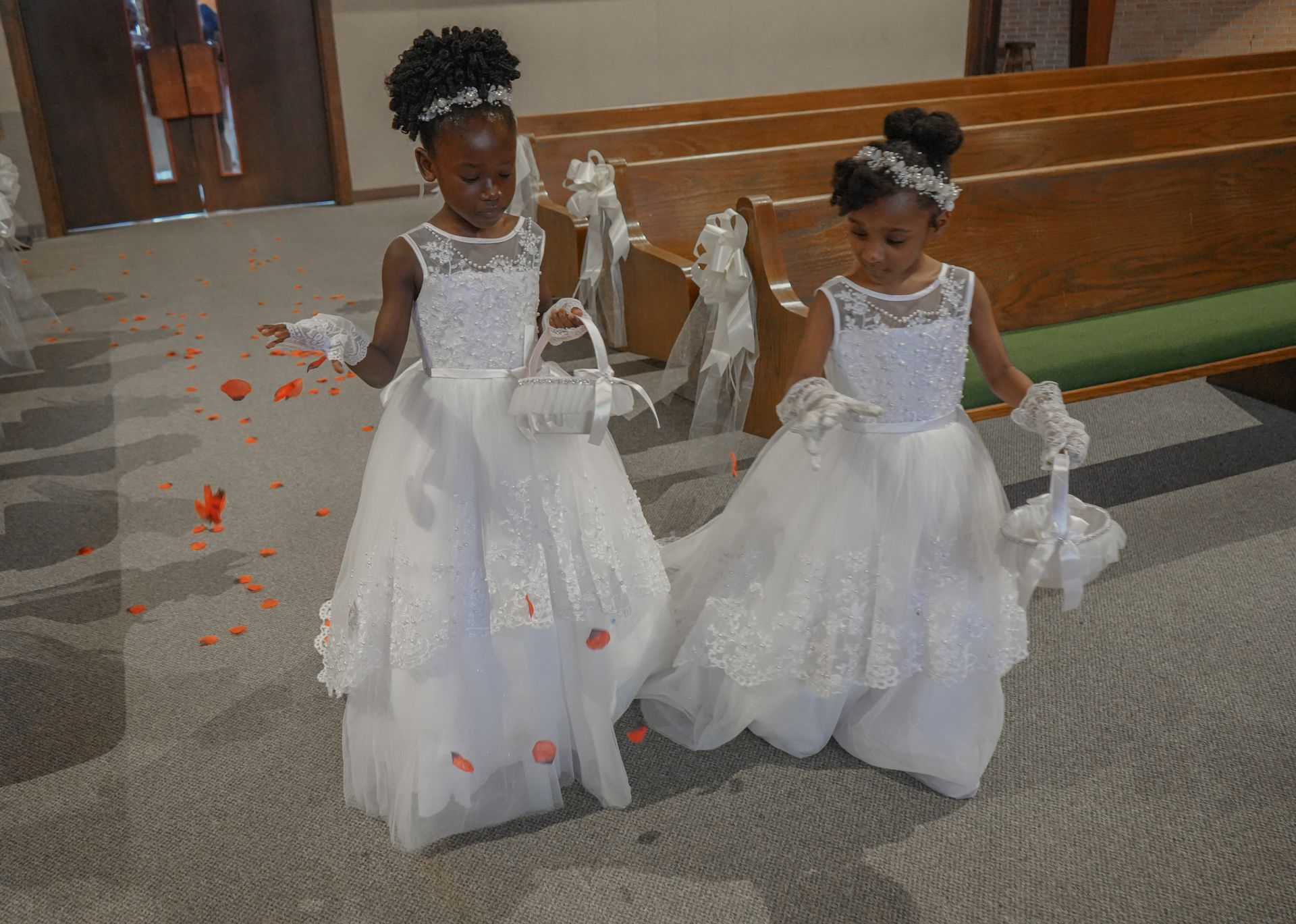 Two flower girls in white dresses are walking down the aisle of a church.