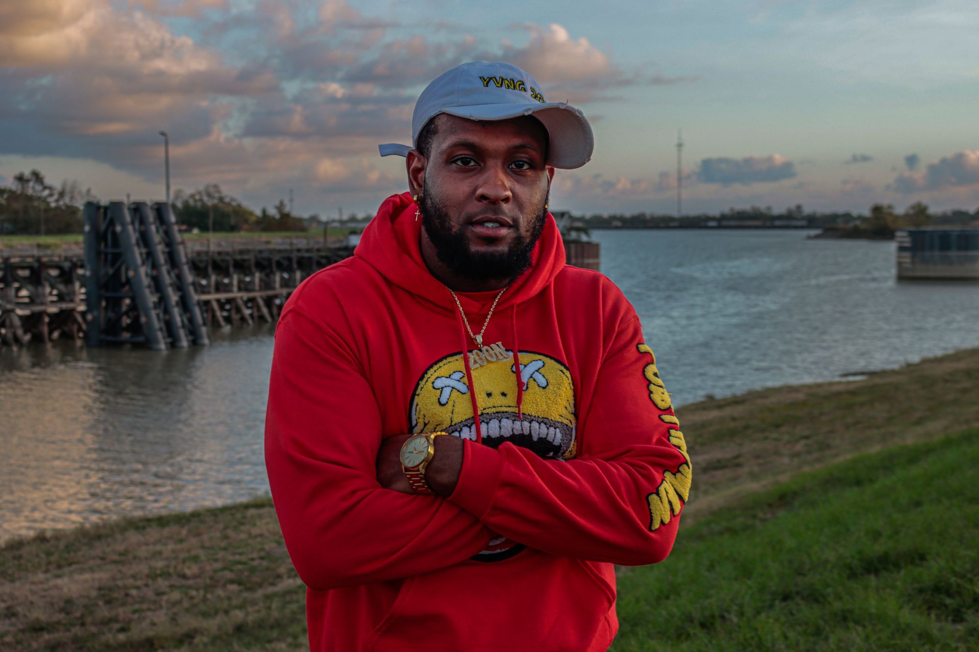 A man in a red hoodie and hat is standing in front of a body of water.
