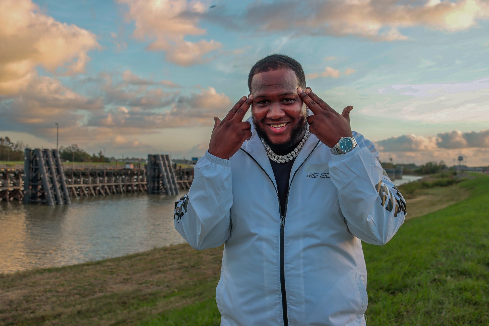 A man in a white jacket is standing in front of a body of water.