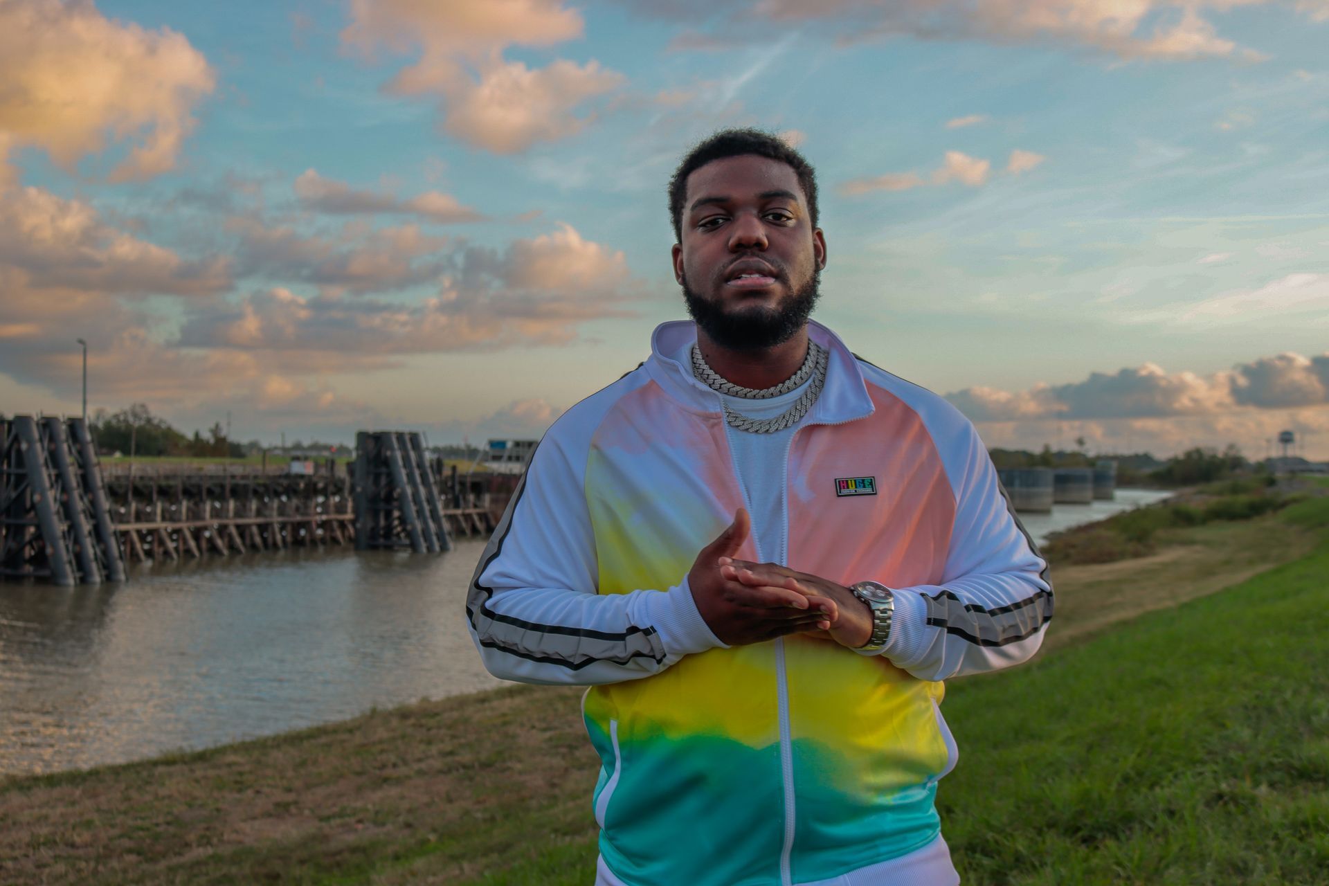 A man in a colorful jacket is standing in front of a body of water.
