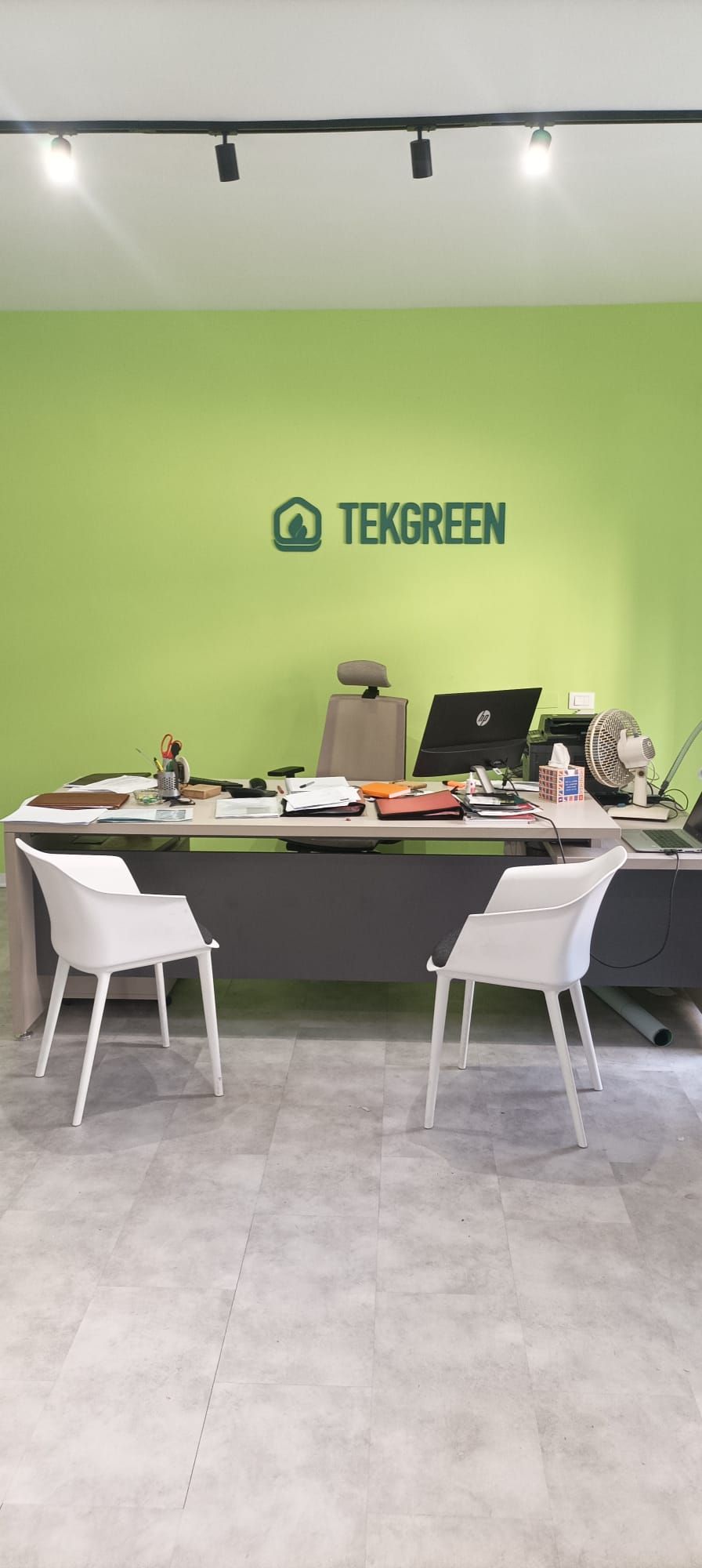 Postazione di lavoro in ufficio con pareti verdi, scrivania, computer portatile, documenti