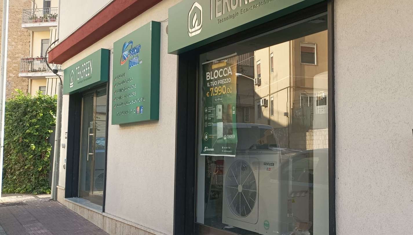 Negozio con vetrina verde, porta e finestre in vetro, situato in un angolo di strada soleggiato.