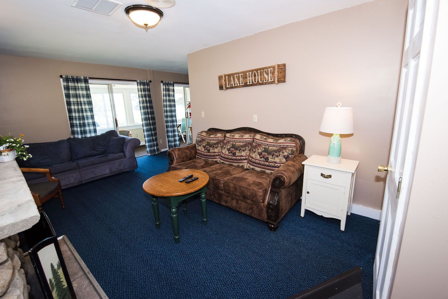 A living room with blue carpet, a dark blue sofa, a patterned brown couch, a wooden coffee table, and a white side table.