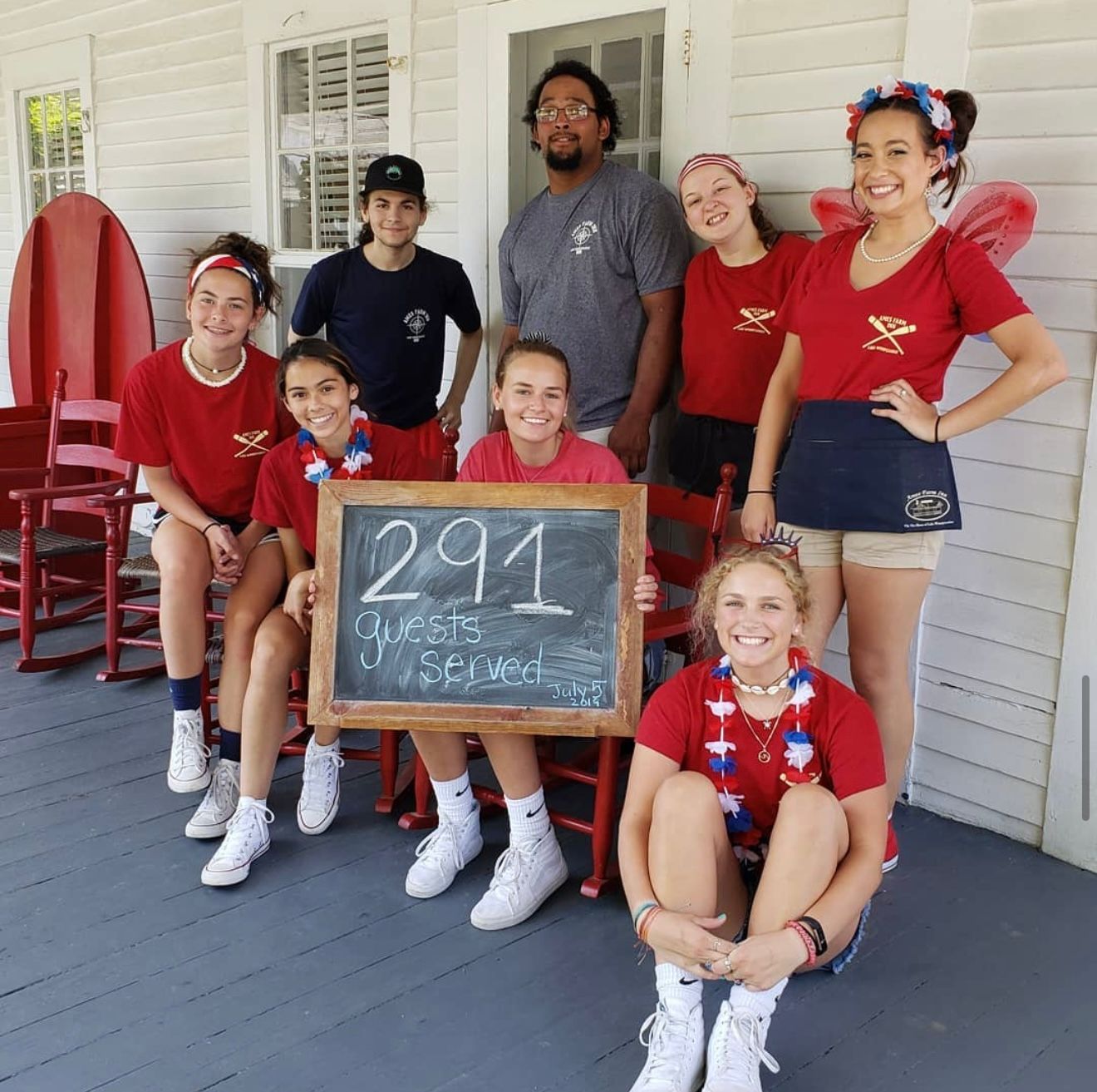 A group of people wearing red shirts on a porch, posing with a chalkboard sign reading 