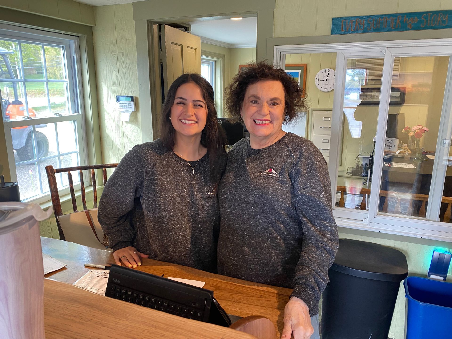 Two people smile while standing behind a wooden service counter in an office setting.