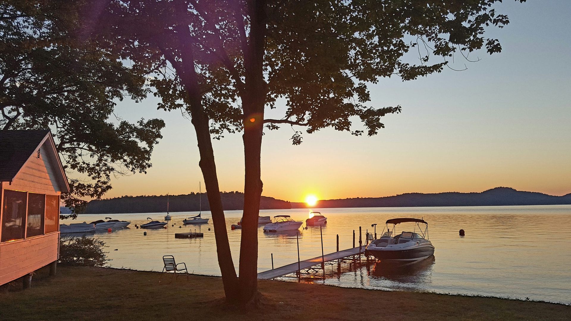 A serene lakefront scene at sunset with a dock, boats, and a house in the background.