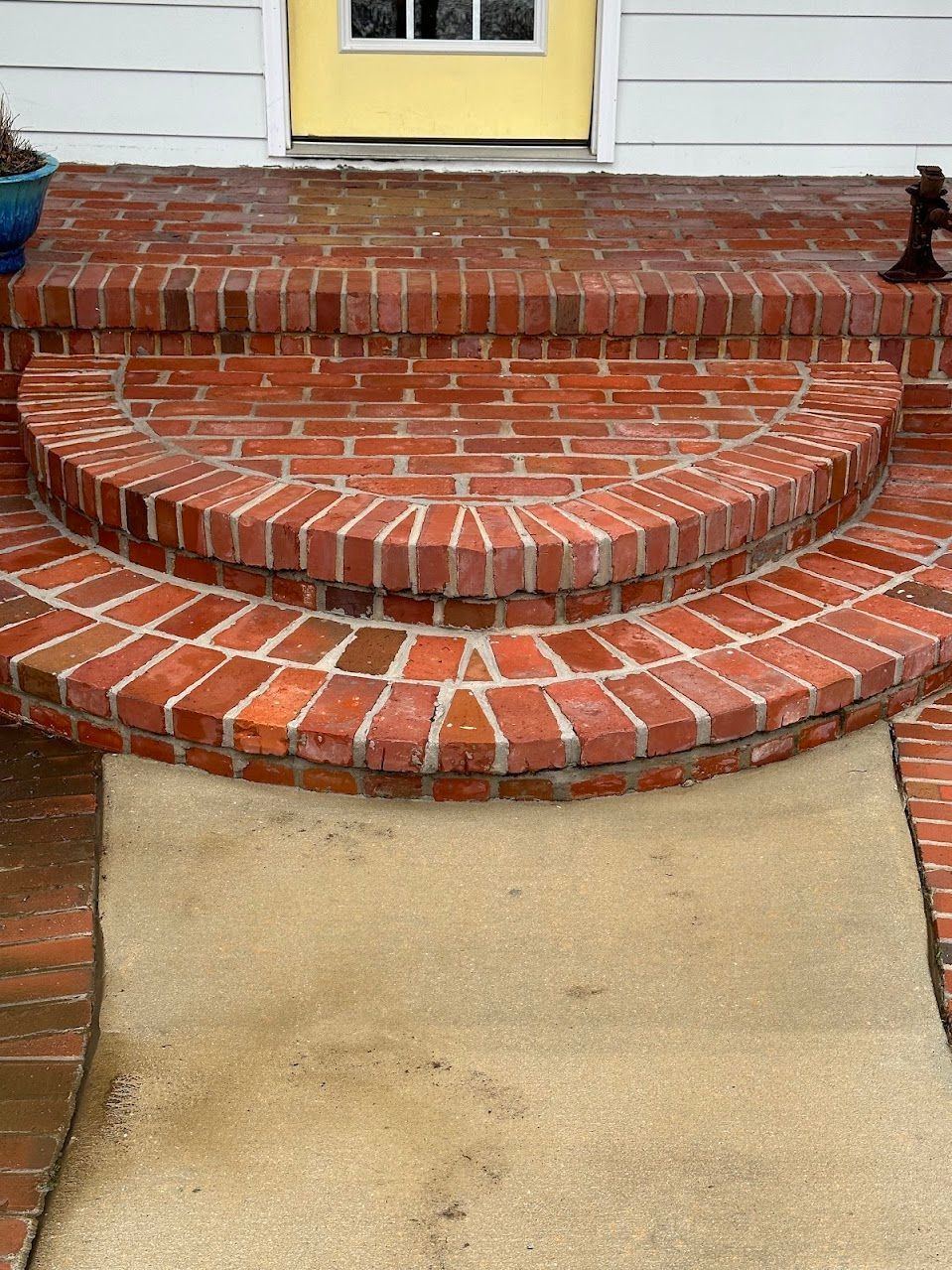 A brick porch with a yellow door and steps leading to it.