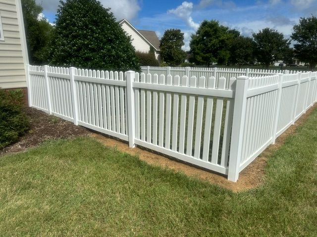 A white fence is sitting in the grass in front of a house.
