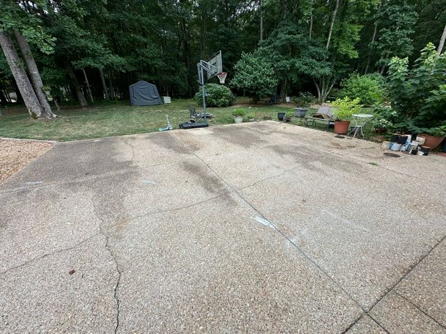 A concrete driveway with a basketball hoop in the backyard.