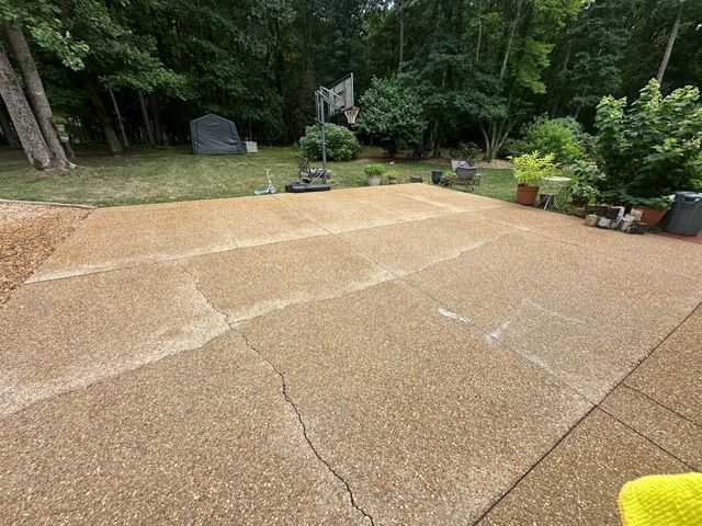 A patio with a basketball hoop in the background and trees in the background.