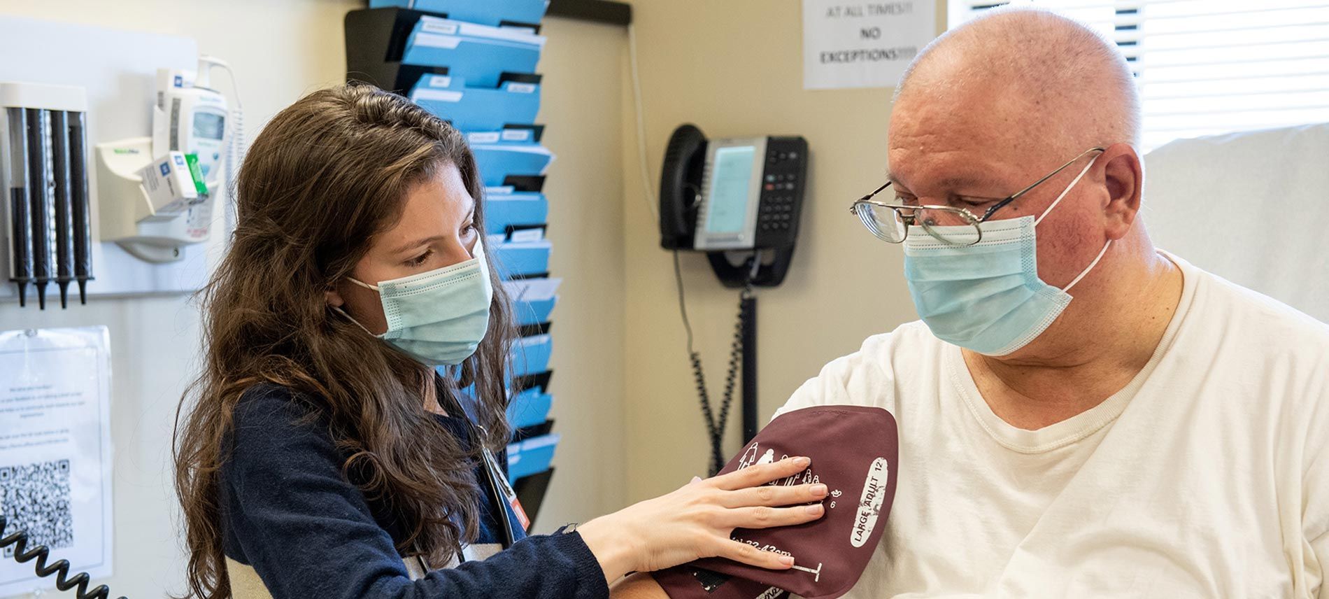 A healthcare worker in a medical office places a blood pressure cuff on a patient's arm.