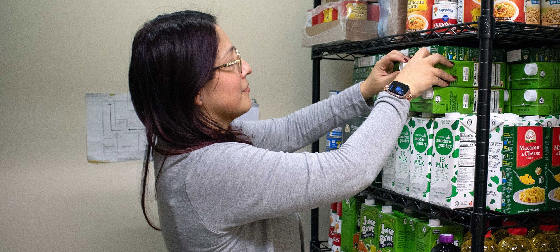 A person wearing a grey sweater reaching to organize green food cartons on a wire shelving unit in a pantry.